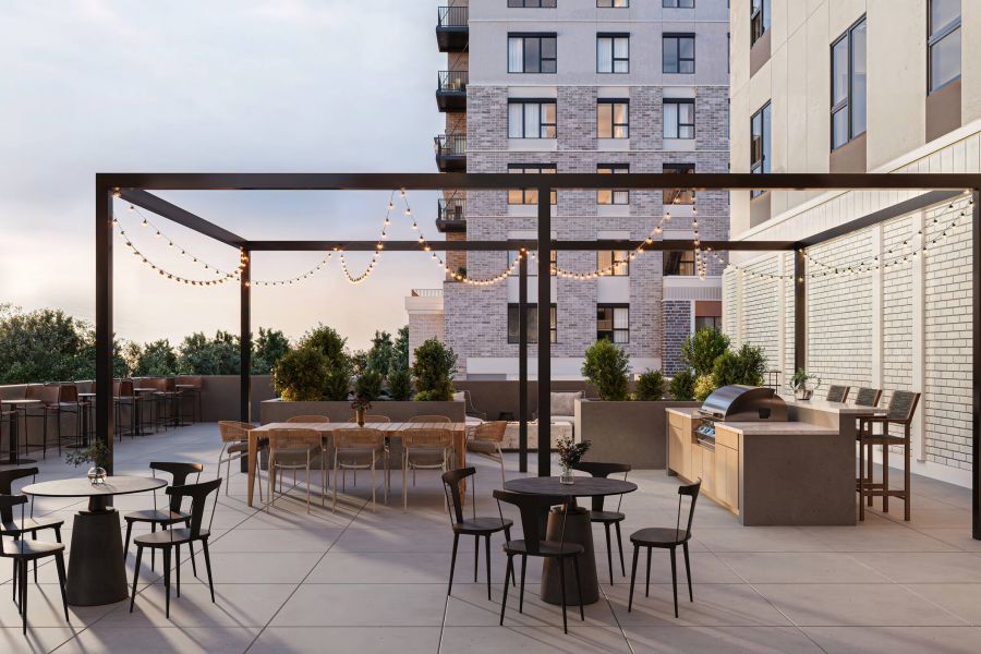 Modern outdoor patio with string lights, dining tables, a grill, and city buildings in the background at Harlow.