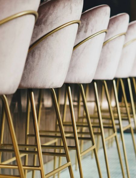 Row of modern bar stools with pink velvet seats and gold metal legs lined up at a bar counter.