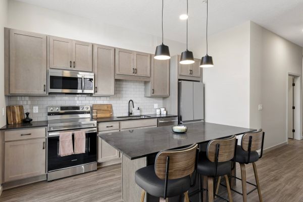 Modern kitchen with light wood cabinets, stainless steel appliances, island, and pendant lights.