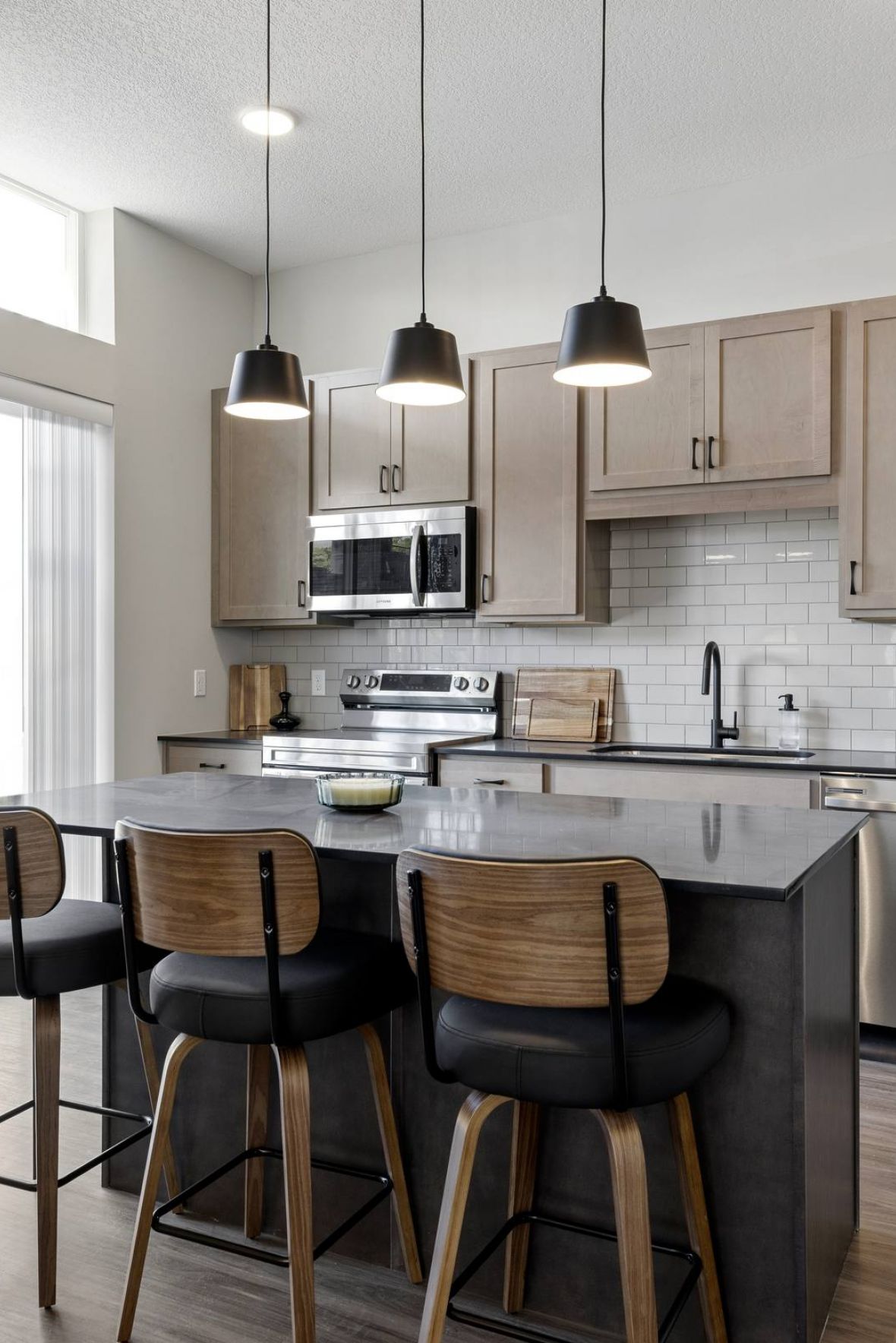 Modern kitchen with island, three bar stools, stainless steel appliances, and pendant lights.
