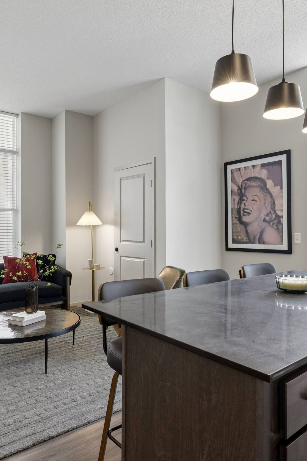 Modern living room and kitchen with a dark island, sofa, large windows, and framed wall art.