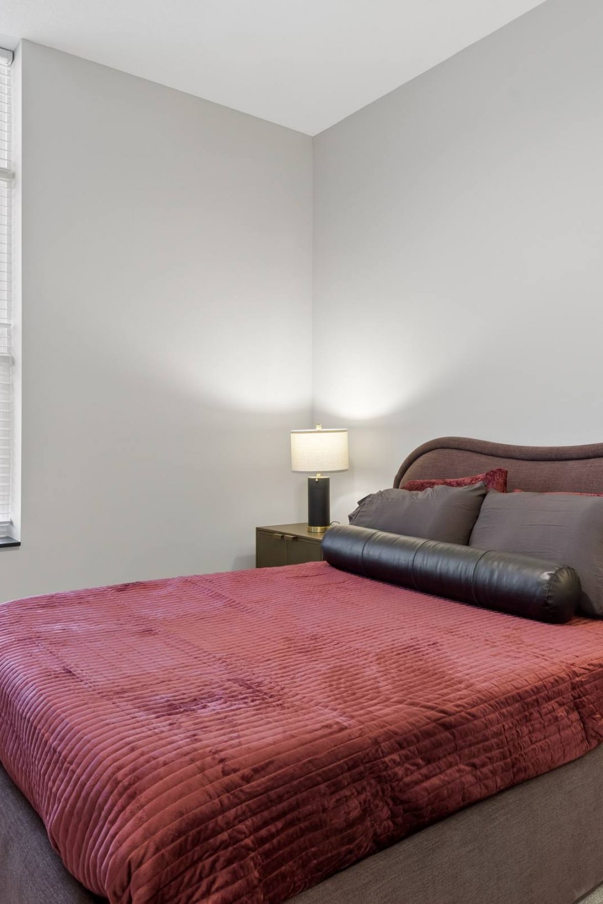 Modern bedroom with a red bedspread, two lamps on nightstands, a tall window, and a potted plant.